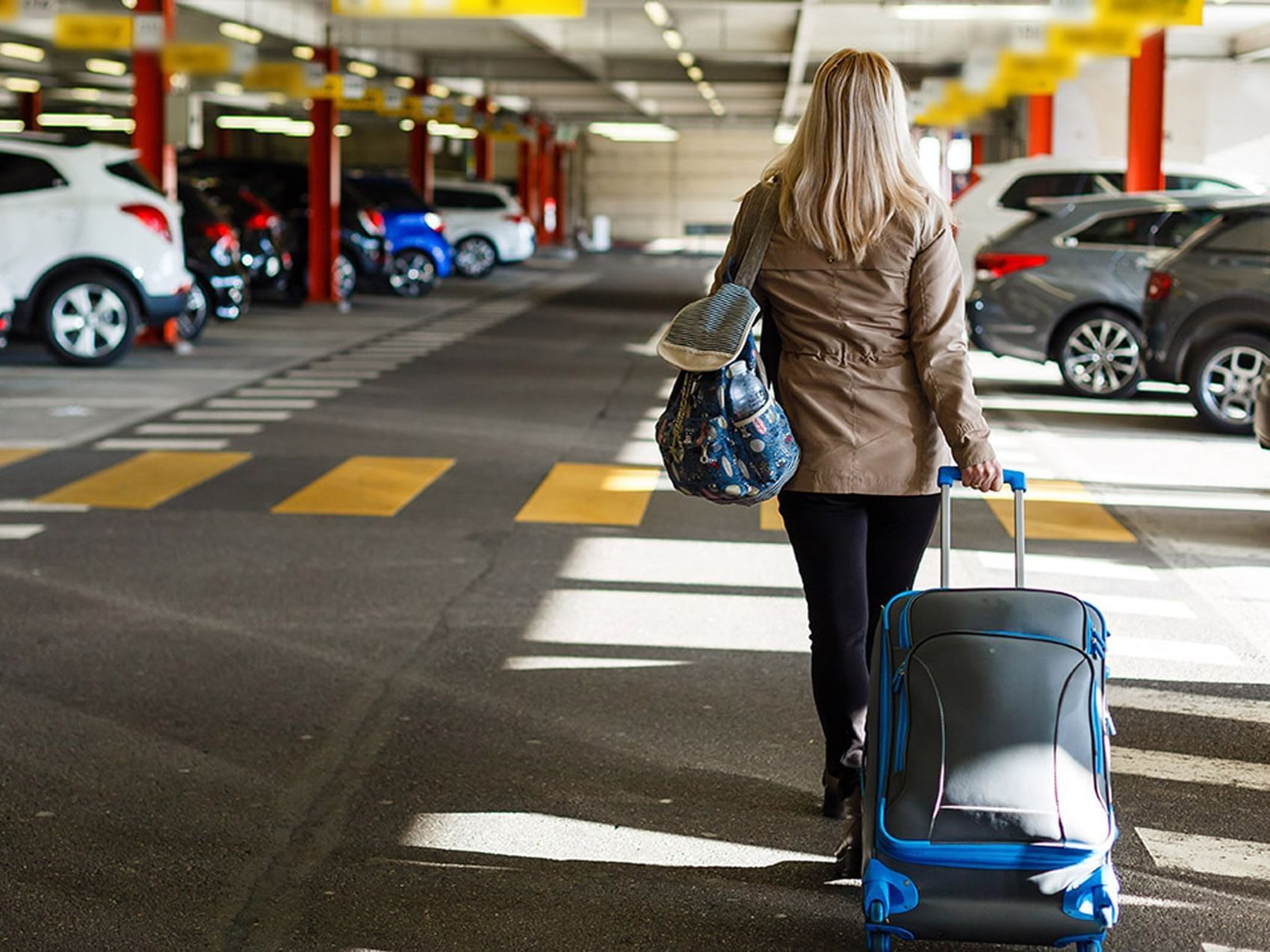 Woman walks through parking garage, pulling suitcase & carrying a bag at D Sabana Hotel, cheap hotels in San Jose Costa Rica