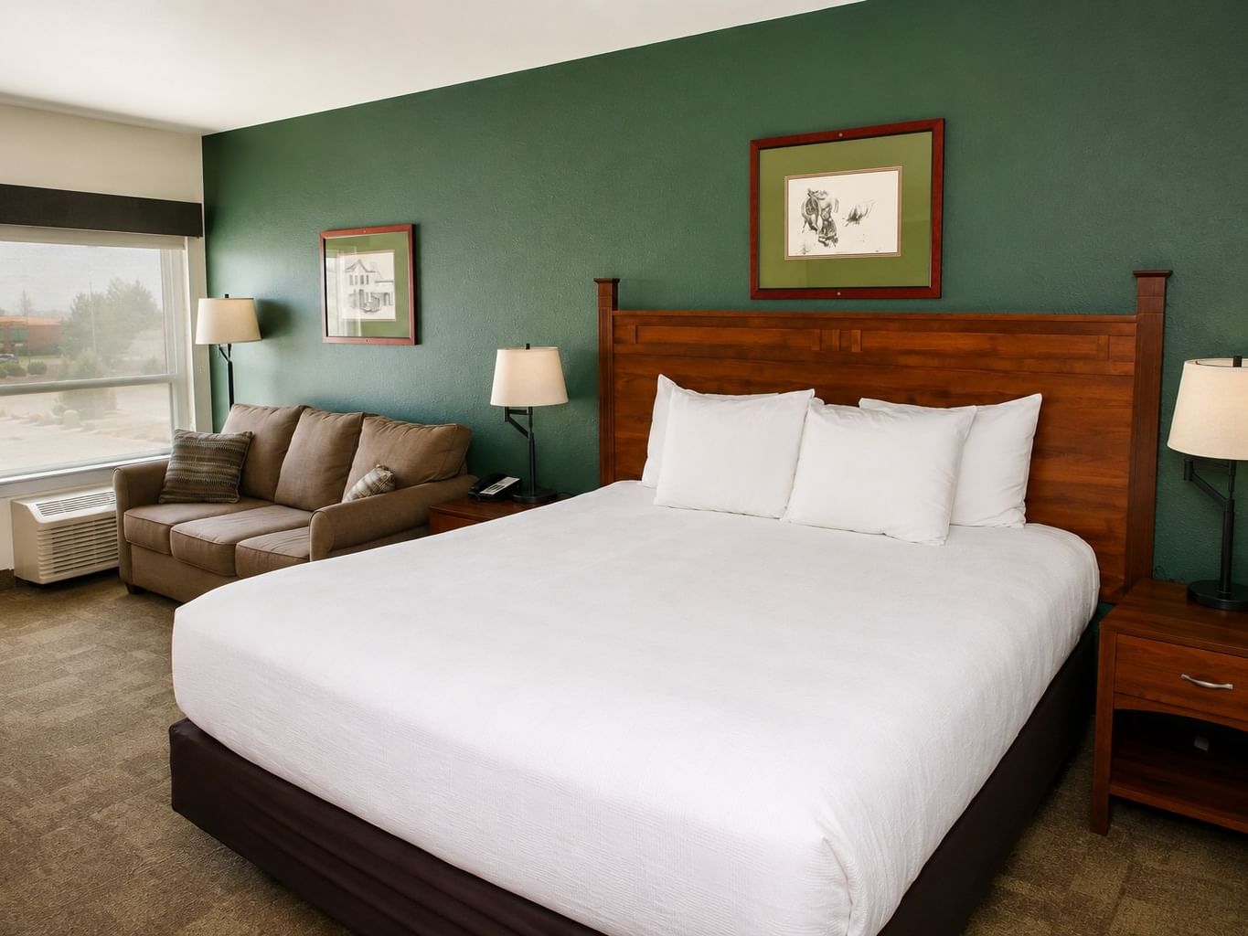 King room with white bedding, wooden headboard, green accent wall, and seating area
