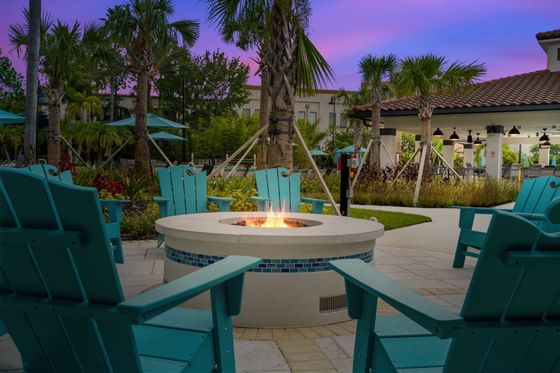 Blue chairs surround a fire pit at the Vista Cay Resort under a purple sky with palm trees.