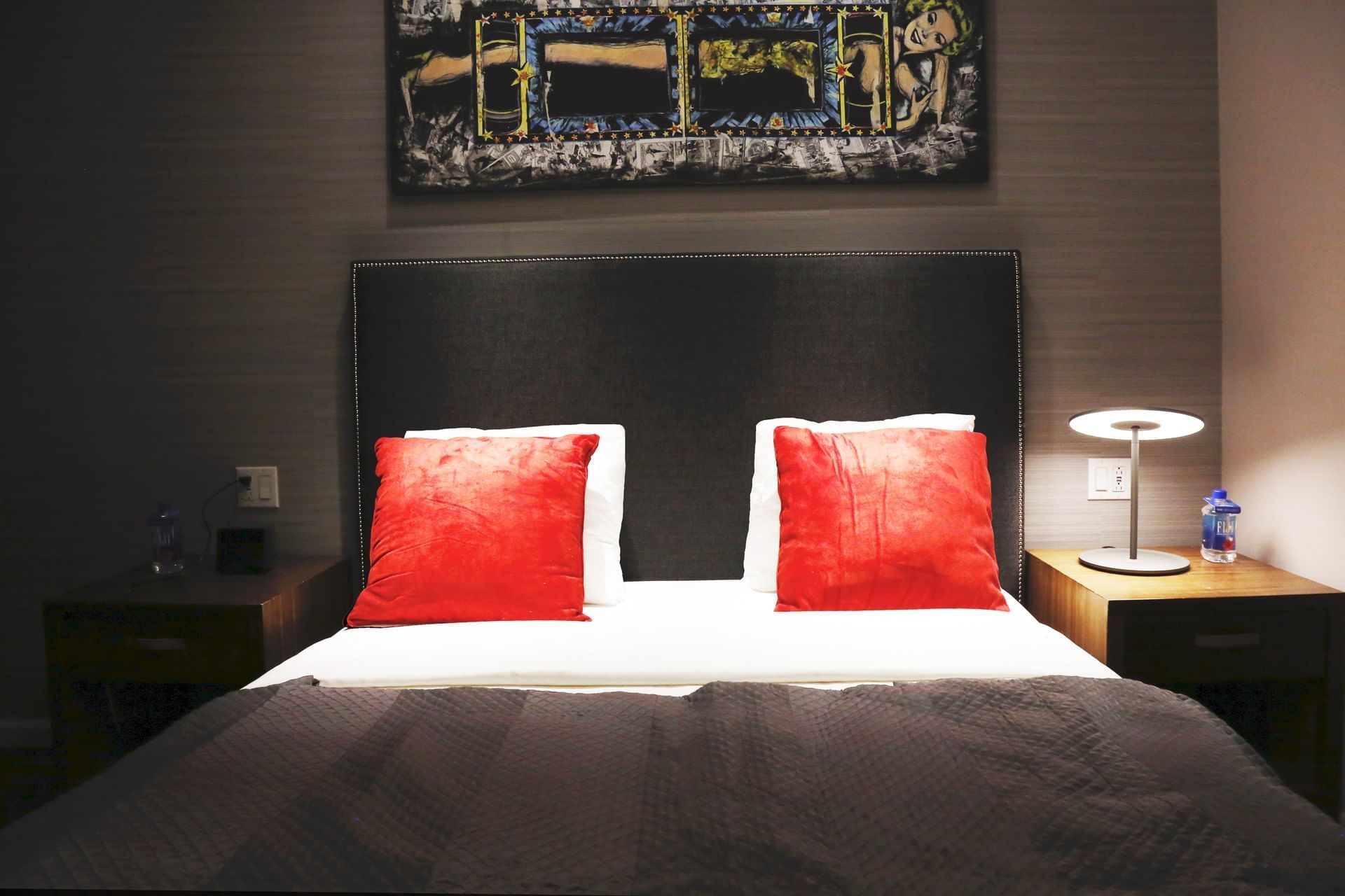 A neatly made bed with red pillows and a black headboard in a hotel room.