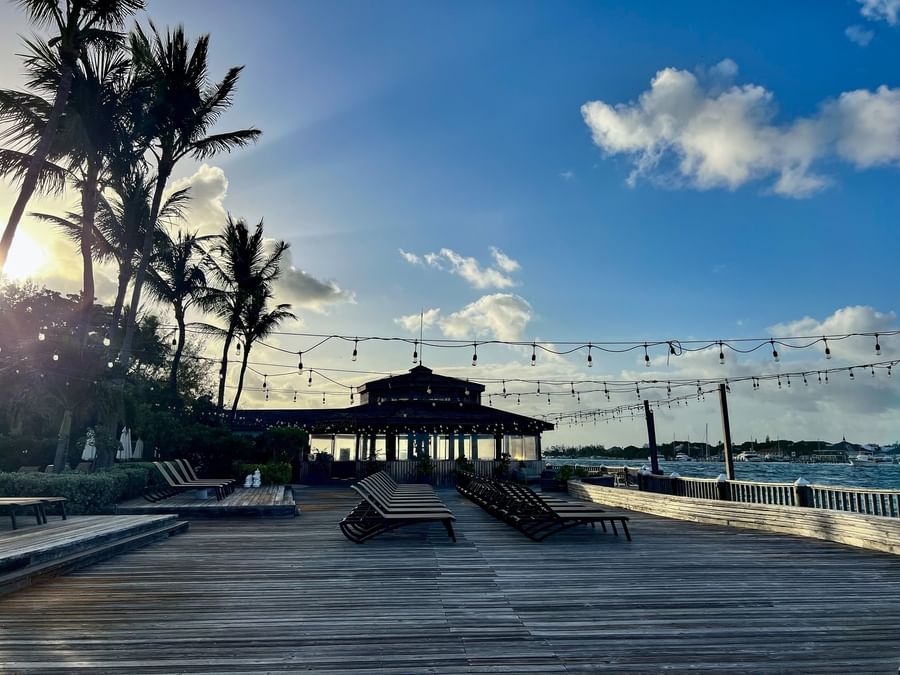 Lounge chairs on a wooden deck by a gazebo under string lights at sunset near Warwick Paradise Island Bahamas