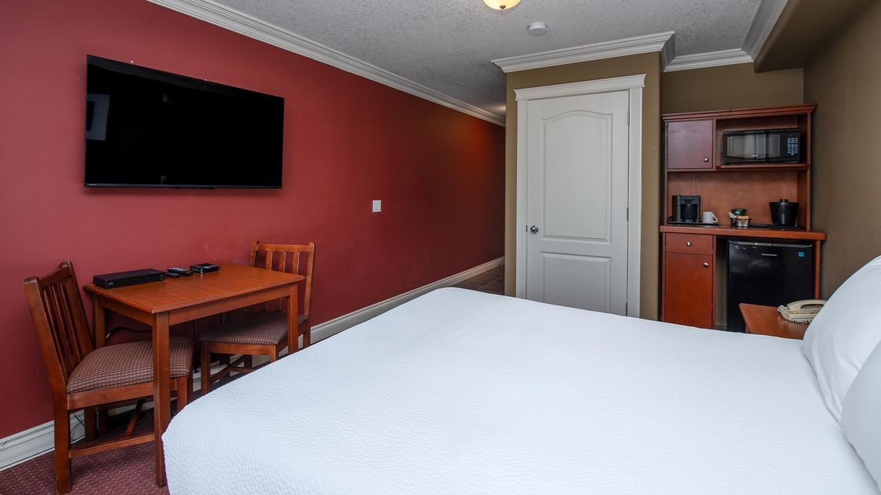 Hotel room with white bed, wooden dining table, wall-mounted TV, and kitchenette at Coast Edson Hotel
