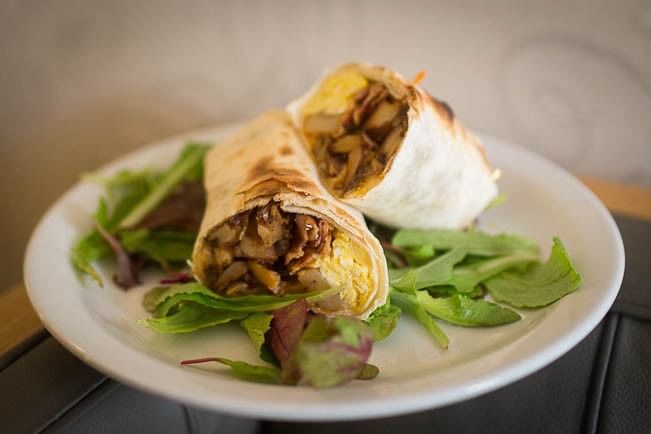Two burritos with scrambled eggs and mushrooms on a plate with greens at Pickwick San Francisco