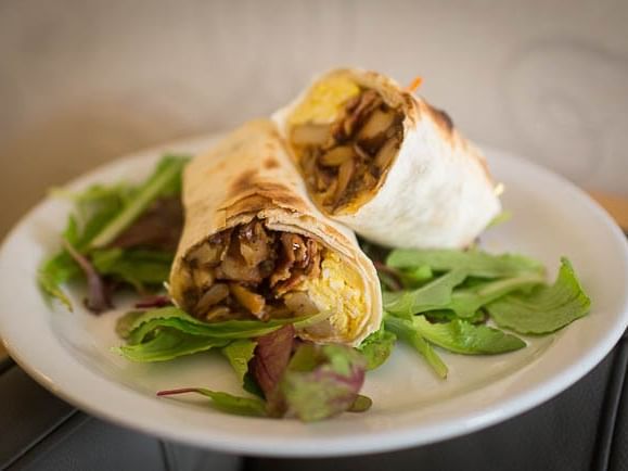 Two burritos on a plate with greens, possibly at a hotel.