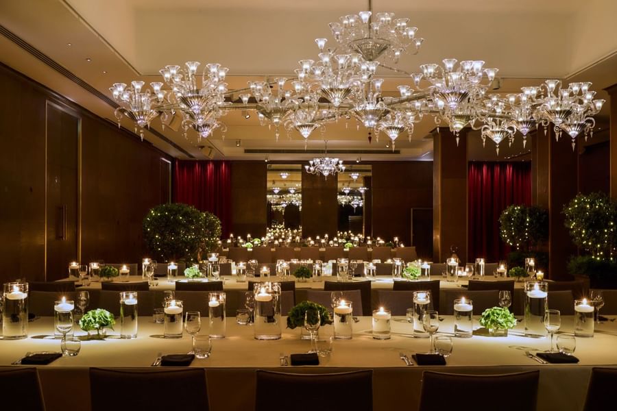 Elegantly arranged dining tables with white candles under a grand glass chandelier in The Crystal Room at The May Fair Hotel