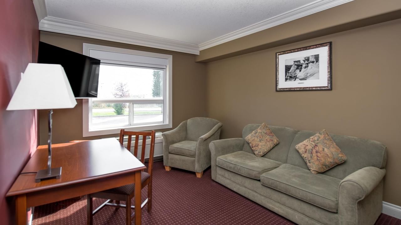 Coast Edson Hotel suite with sage green sofa, armchair, work desk, and large window with natural light.