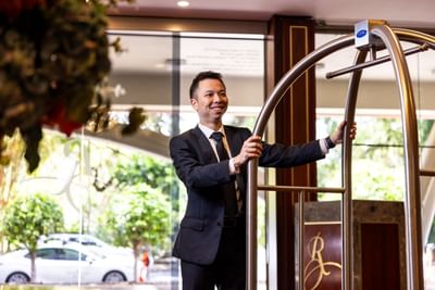 A friendly and helpful bellhop standing with a luggage cart at the Royal on the Park Hotel