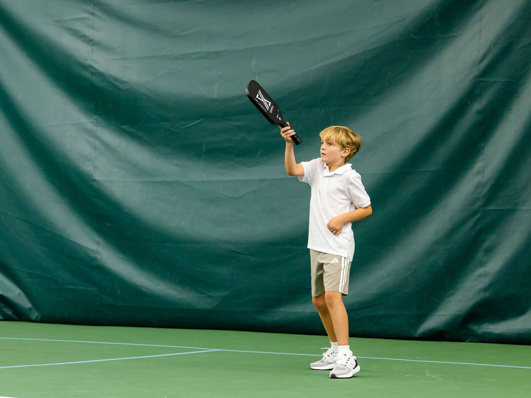 A young boy playing pickleball with a paddle on a court.