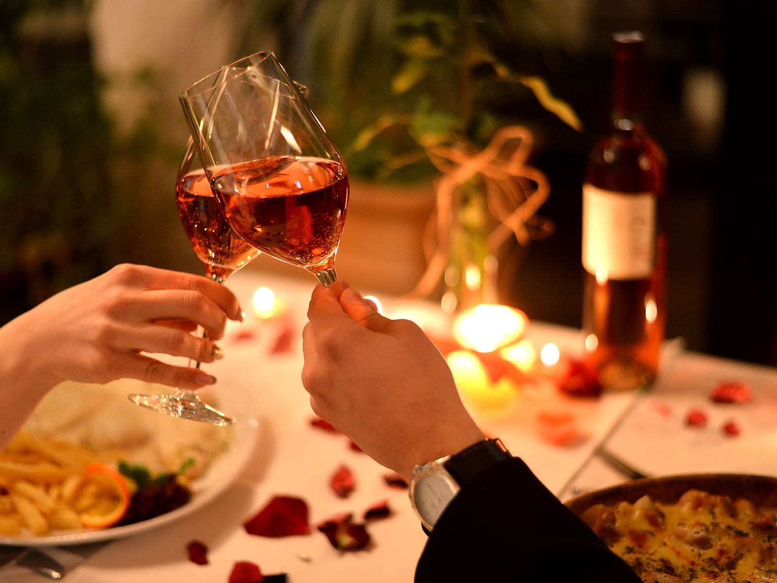 Hands toasting with wine glasses over a romantic dinner setup with candles and plates.