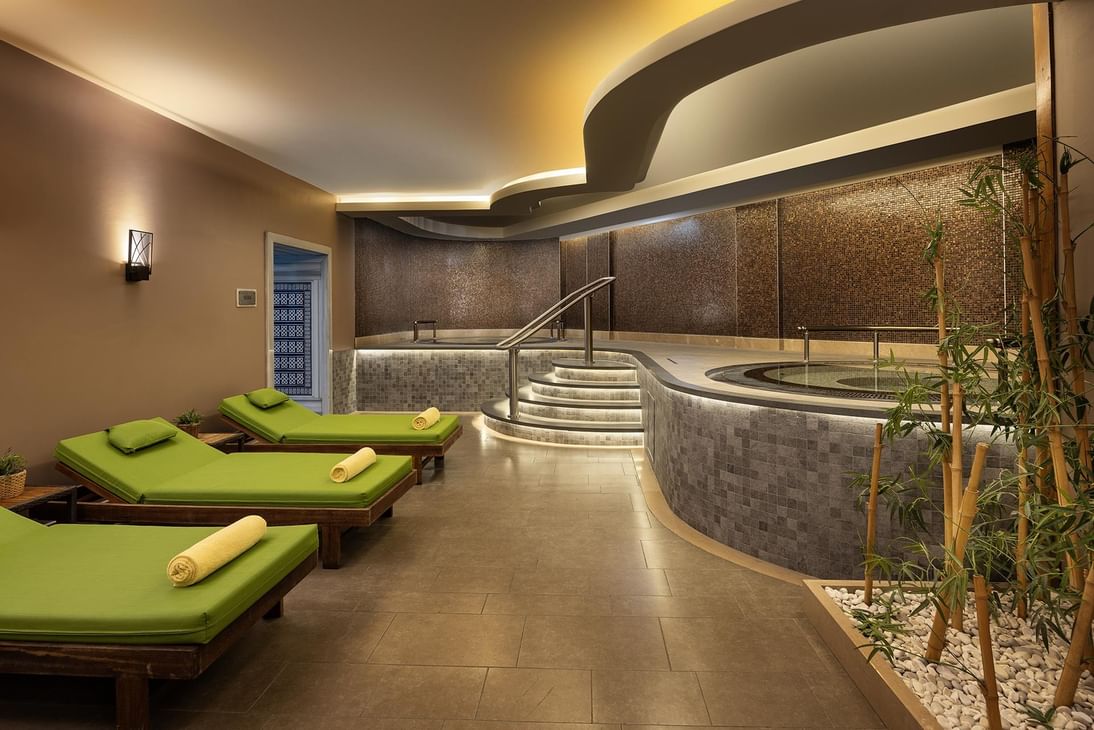 Green loungers by a tiled pool under a curved ceiling in a spa at Titanic Business Kartal
