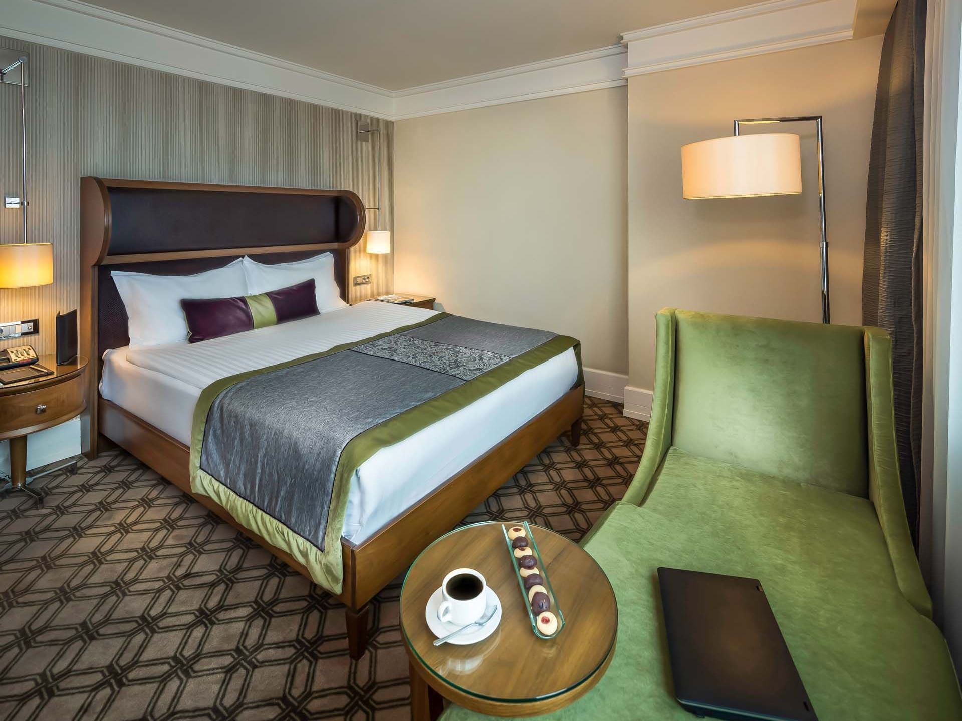 Titanic Port Bakırköy'deki Superior odada çift kişilik yatak, yan lambalar, yeşil berjer ve sehpa bulunmaktadır.