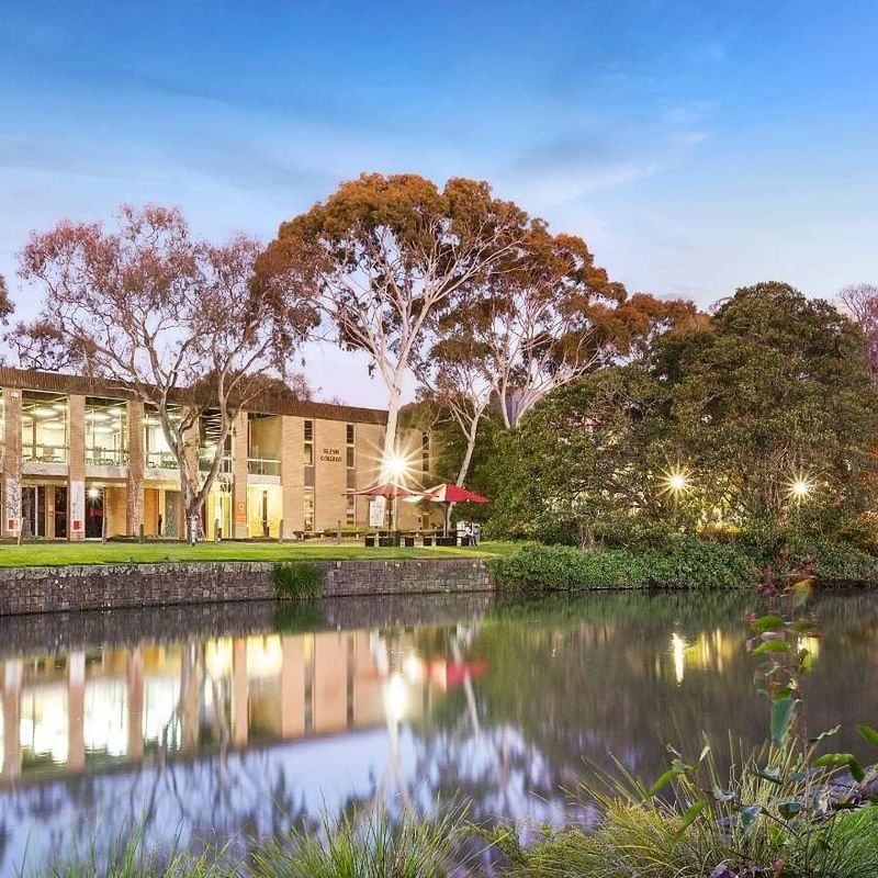 La Trobe University Glenn College building by a serene pond at dusk.