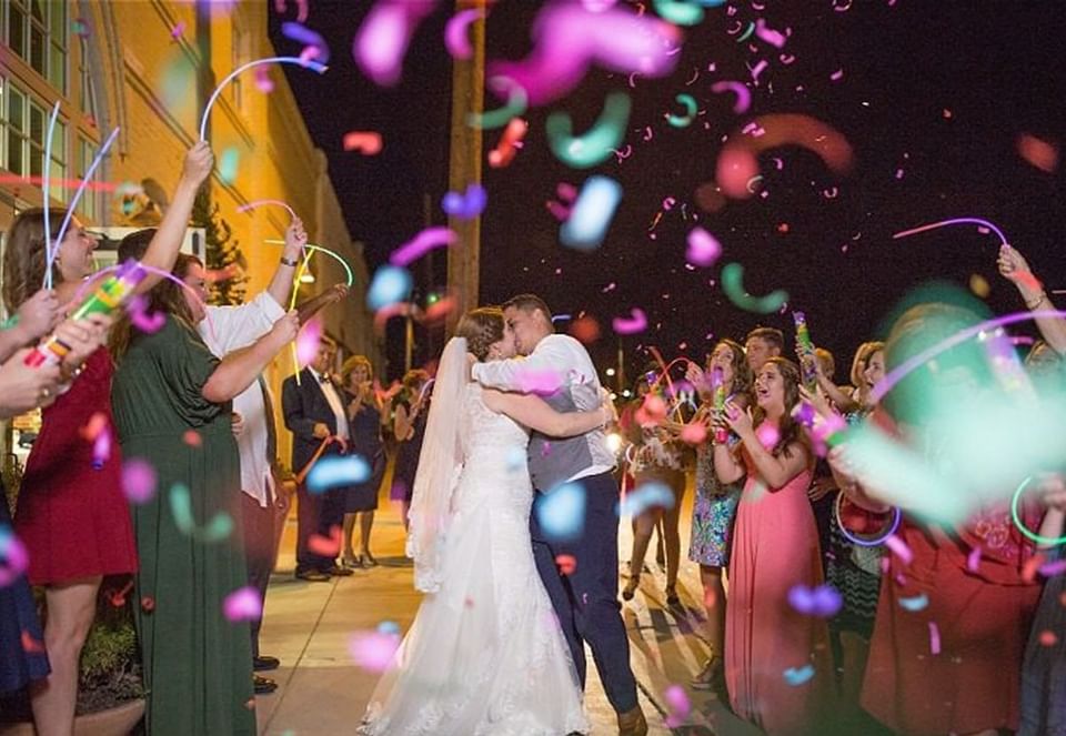 Wedded couple kissing under a rain of confetti outdoors in Inn at the Crossroads