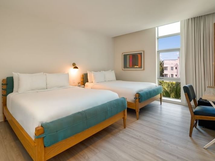 Bedroom Double Queen with two queen beds, teal accents, a window view, and a desk at Kenmore Village Hotel South Beach