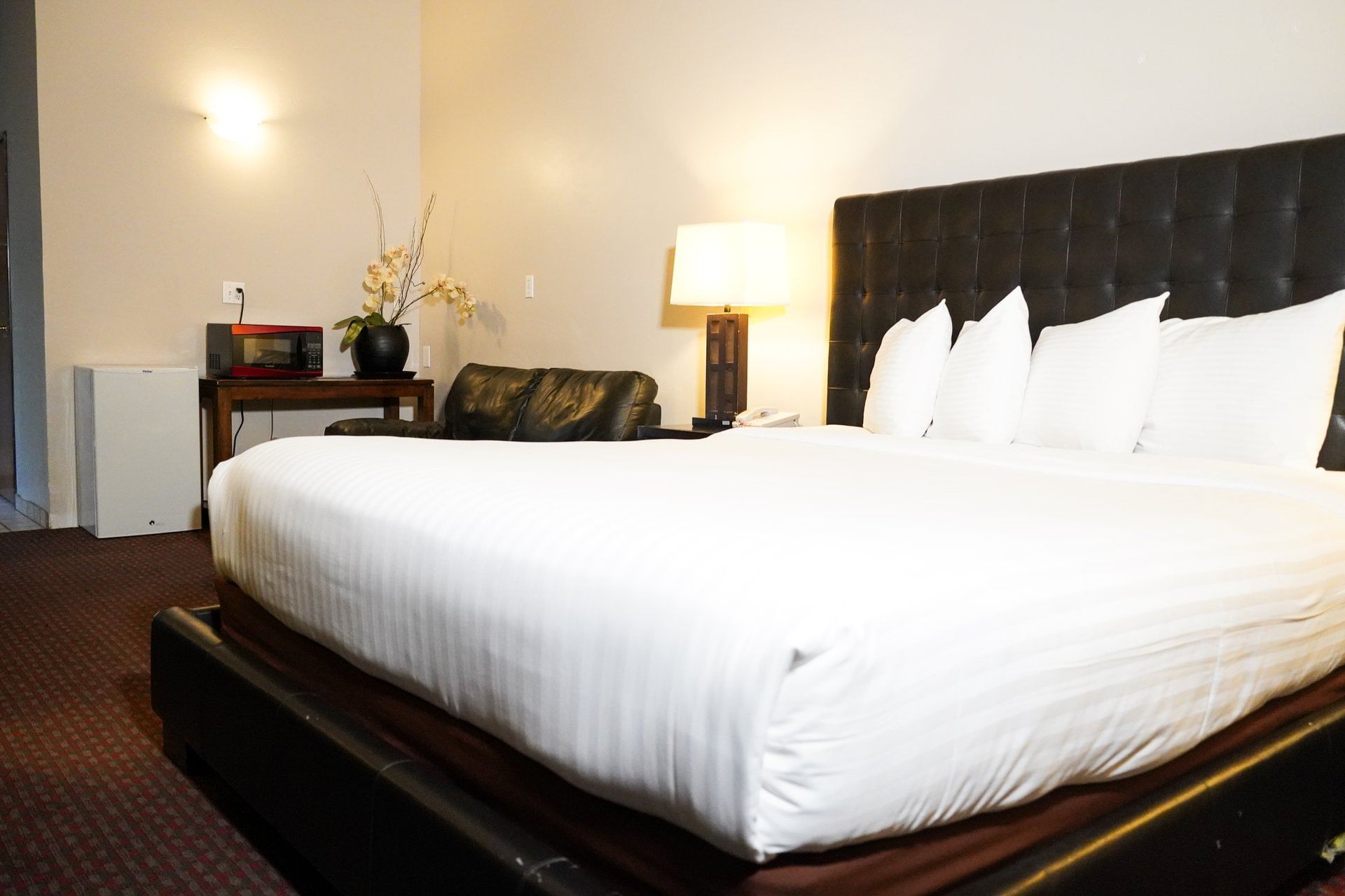 A hotel room with a large bed, dark leather headboard, and white bedding.