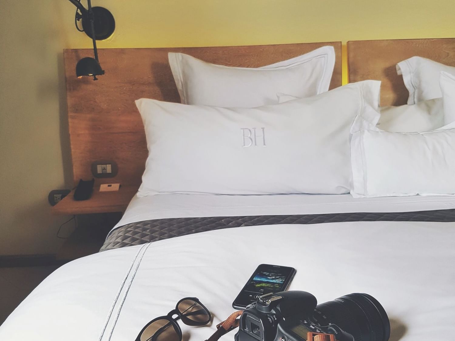 Cozy bed with white pillows, bedside lamp, and travel essentials resting on the covers at Billini Hotel Historic Luxury