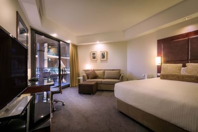 Bedroom with TV, sofa & balcony view at Amora Hotel