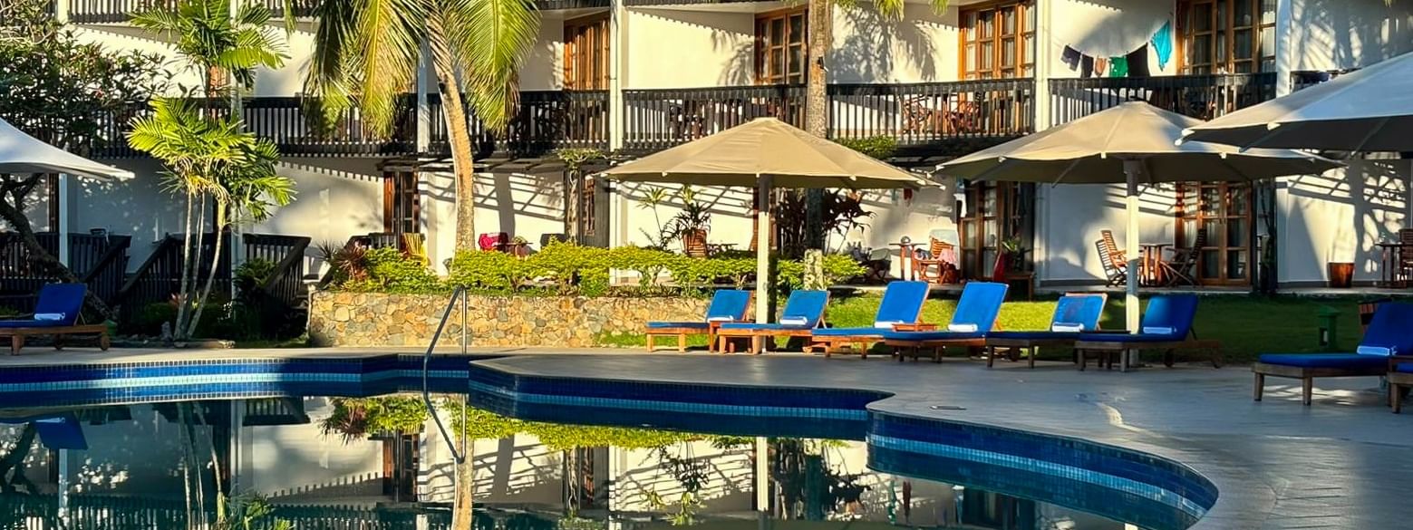 Blue swimming pool with beach chairs under umbrellas in front of resort building at Warwick Fiji Resort and Spa Korolevu