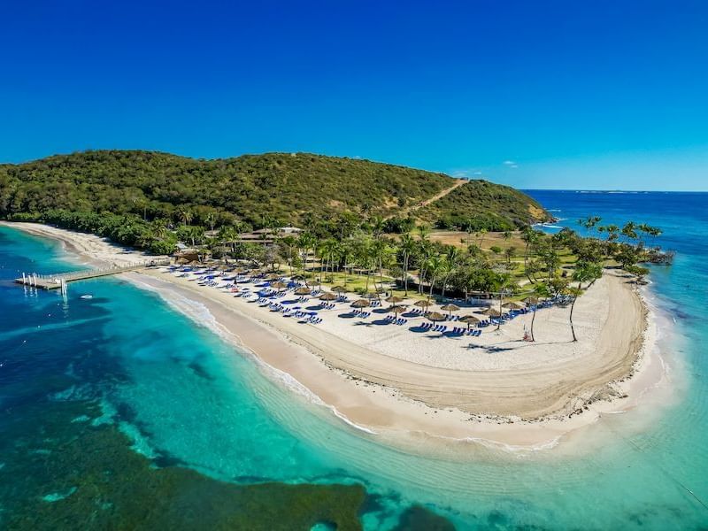 Aerial view of a serene beach with lounge chairs, clear turquoise water, and lush greenery near El Conquistador Resort