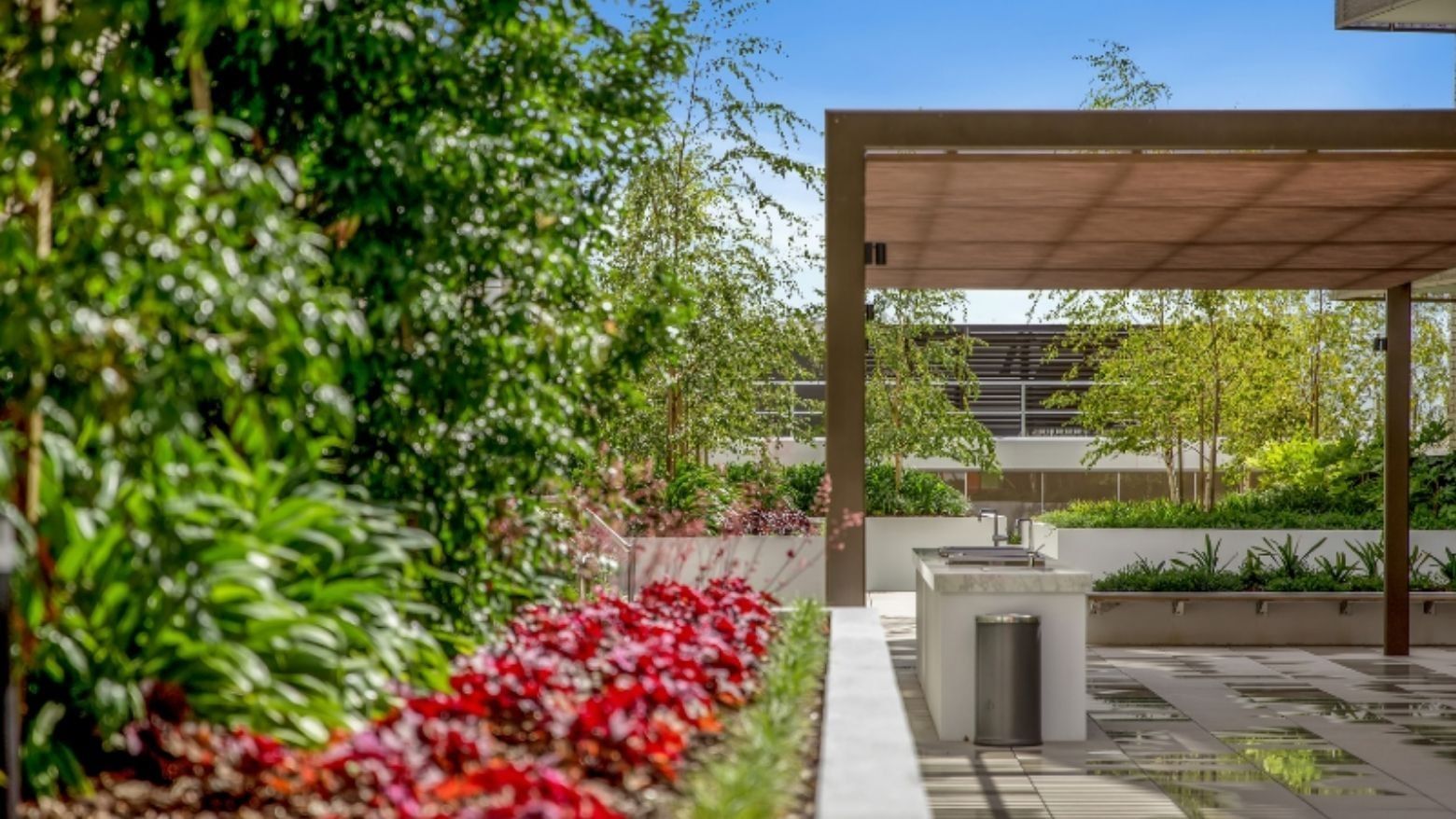 Outdoor garden with canopy, red flowers, greenery, and a covered area with a barbeque.