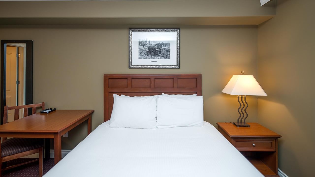 Coast Edson Hotel guest room with white bedding, wooden furniture, and framed artwork above headboard.