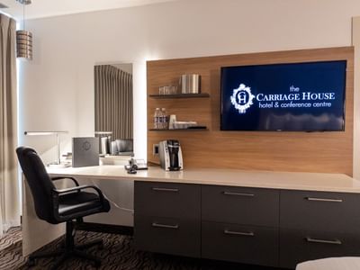 Desk with coffee maker and TV displaying Carriage House logo at Carriage House Hotel & Conference Centre.