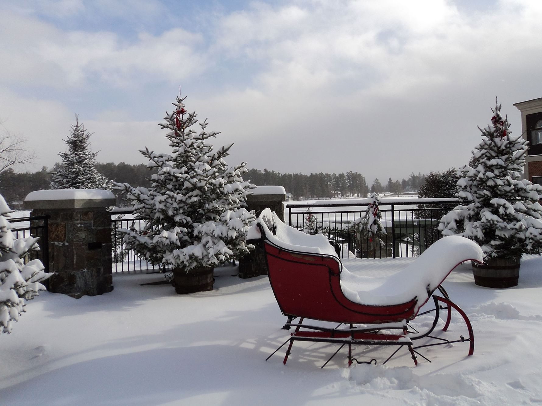 Snowy scene with a red sleigh and Christmas trees on a terrace.