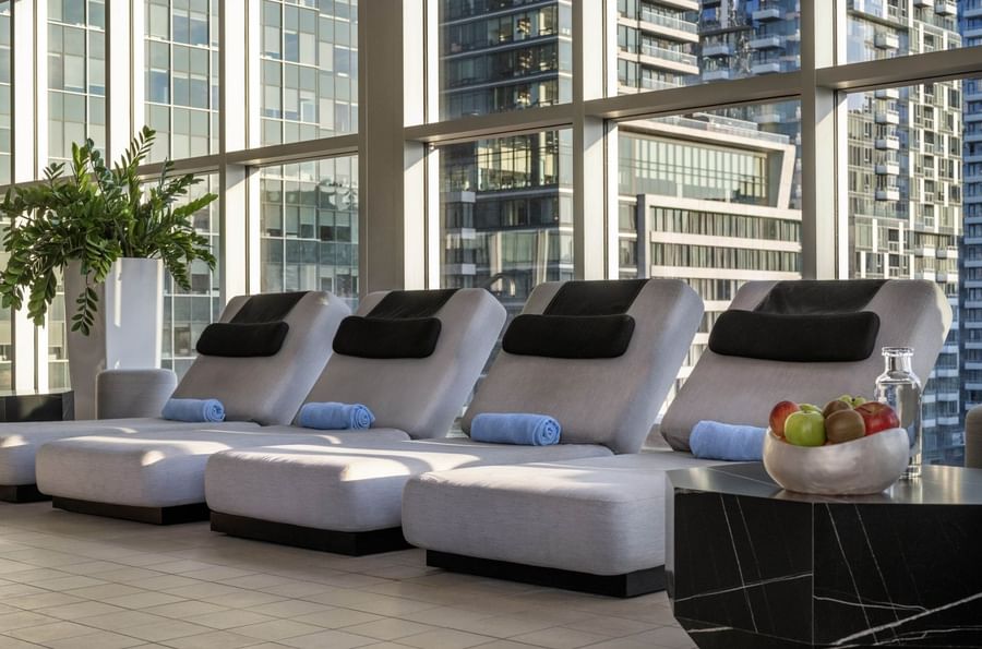 Modern grey lounge chairs with blue towels by floor-to-ceiling windows in indoor pool at Warwick Le Crystal