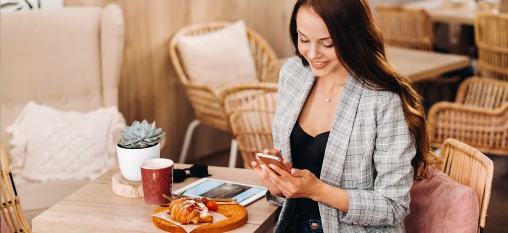 Woman in a café, with a pastry, coffee and tablet on the table.