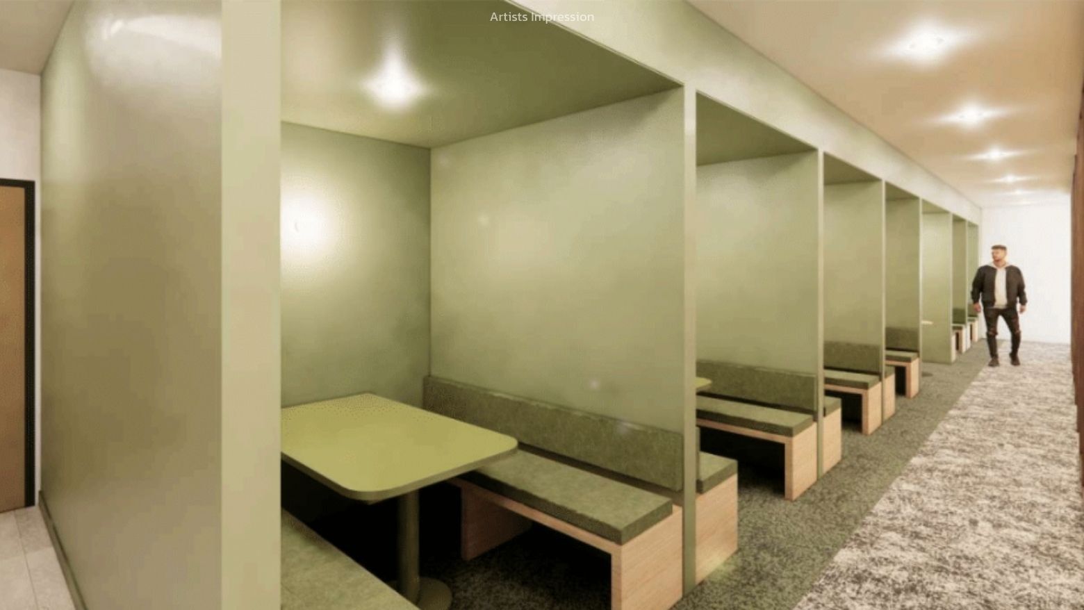 Man walking past a long row of green cubicles with tables and benches at UniLodge Brisbane City.