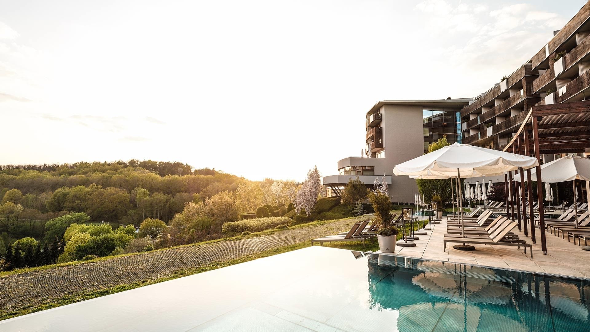 A modern resort building overlooking a pool with lounge chairs and umbrellas at Falkensteiner Balance Resort Stegersbach