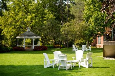 White Adirondack chairs arranged on a grassy lawn near a wooden gazebo at Spencer Hotel & Conference Centre