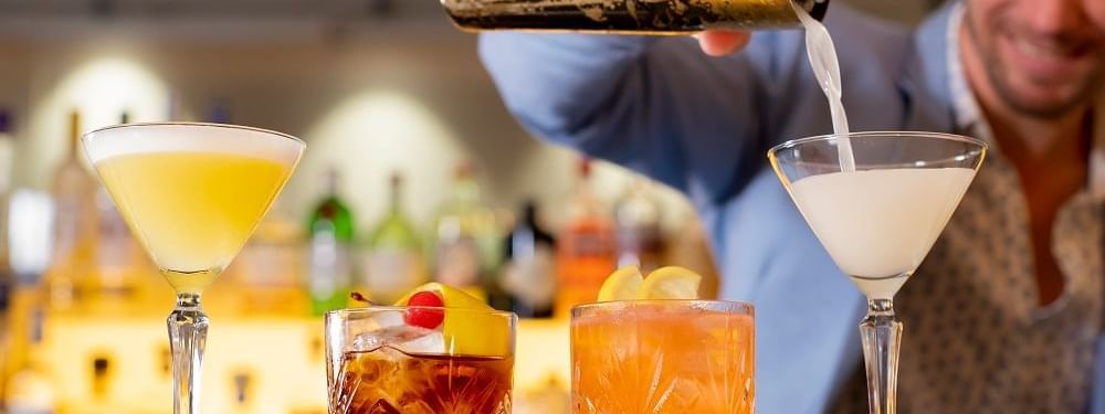 Bartender pouring a white cocktail into a martini glass beside three vibrant drinks at Novotel Sydney International Airport