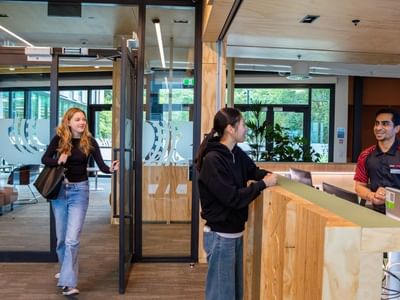 Guest entering modern hotel lobby with wooden reception desk and staff member greeting another visitor at Tupuārangi.