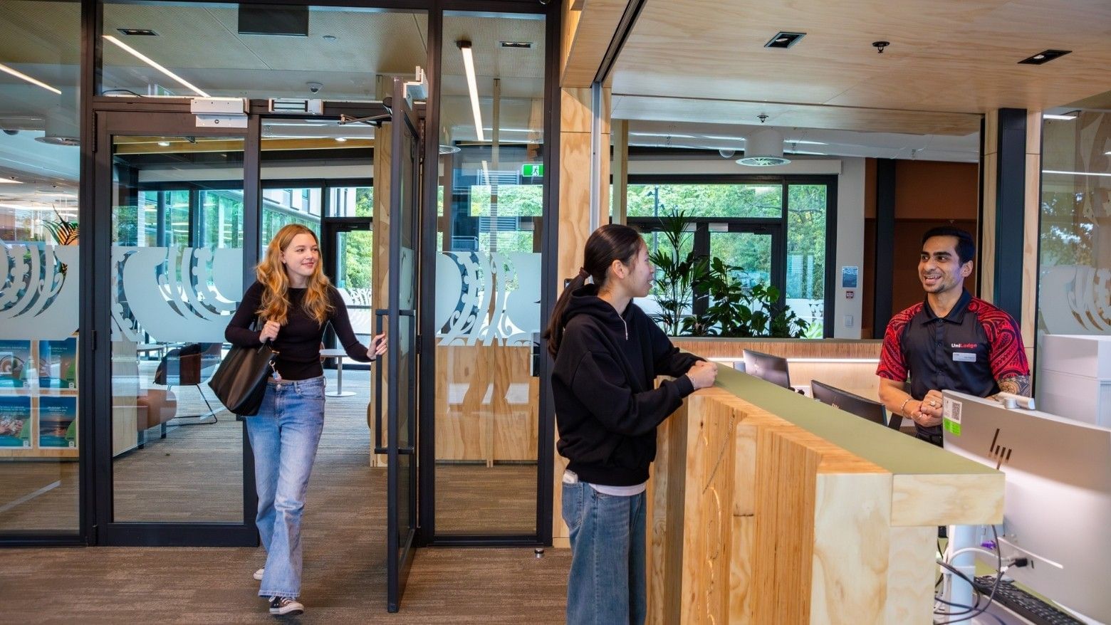 Guest entering modern hotel lobby with wooden reception desk and staff member greeting another visitor at Tupuārangi.