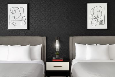 Two beds with white pillows and artwork on black walls at ArtHouse Hotel New York City.