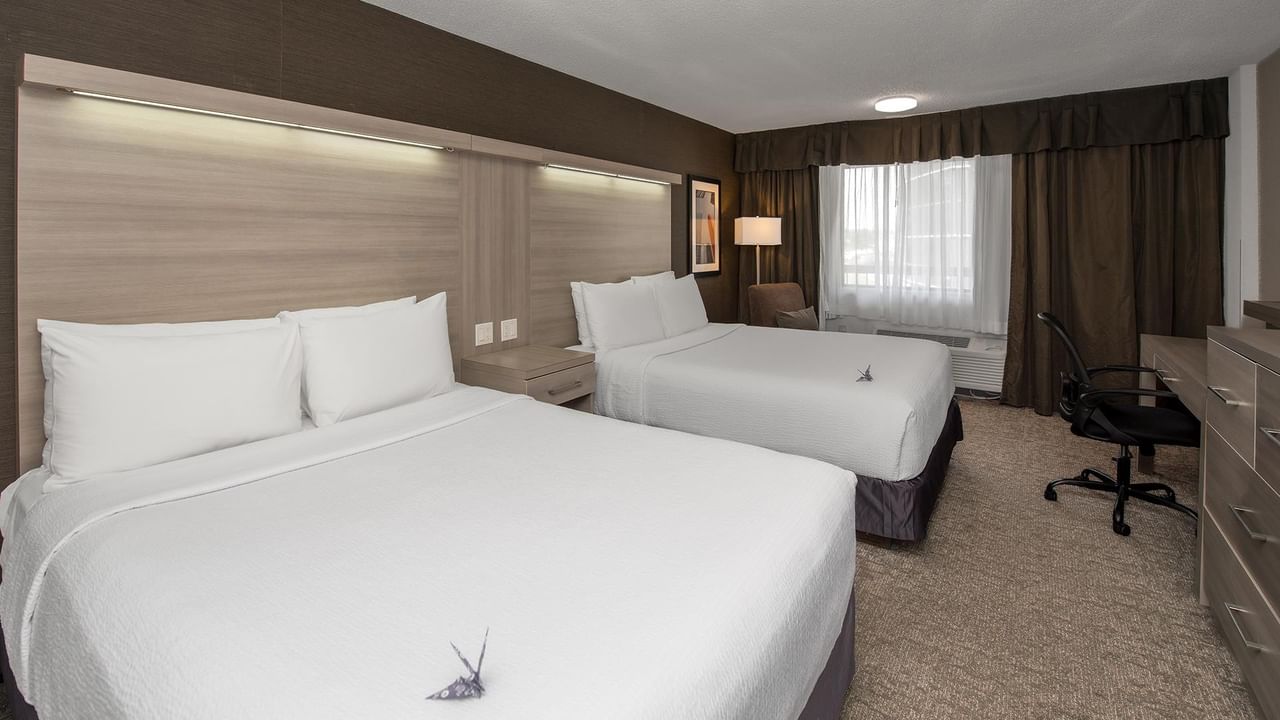Modern hotel room with two queen beds, white linens, desk chair, and window with curtains at Coast Calgary University Area Hotel by APA
