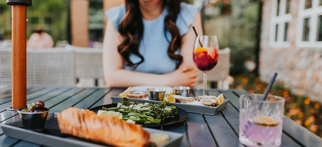 Outdoor table at hotel patio set with a plate of asparagus, oysters, bread and two cocktails.