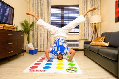 Guest playing a game of Twister doing a handstand in the bright living room of his apartment at Tradewinds Apartment Hotel