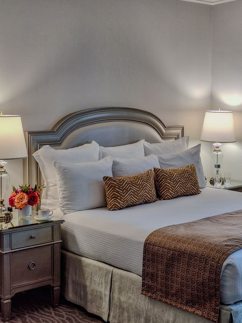 Classic King features King bed with bronze pillows by a side table under a bright bedside lamp at Warwick Melrose Dallas