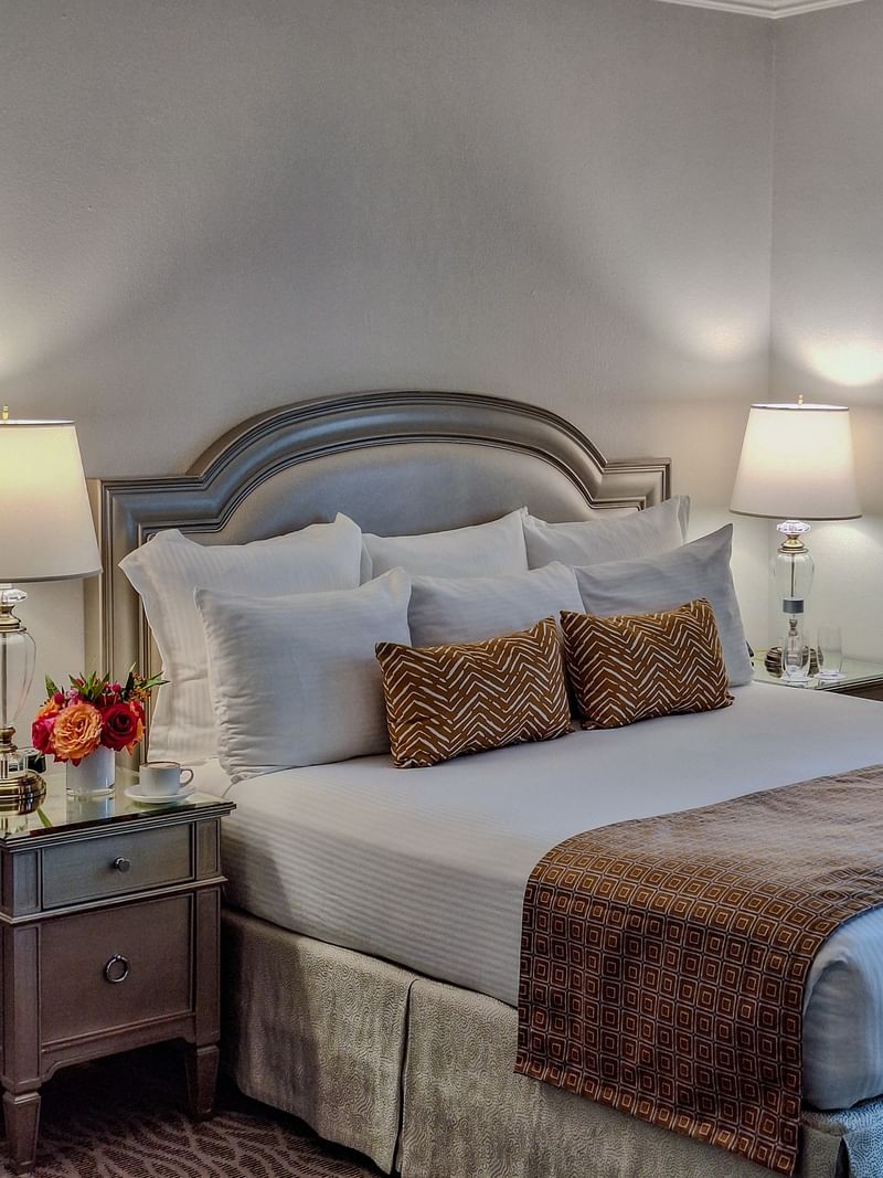 King bed with brown and white pillows and a flower vase on the nightstand at Warwick Melrose Dallas.