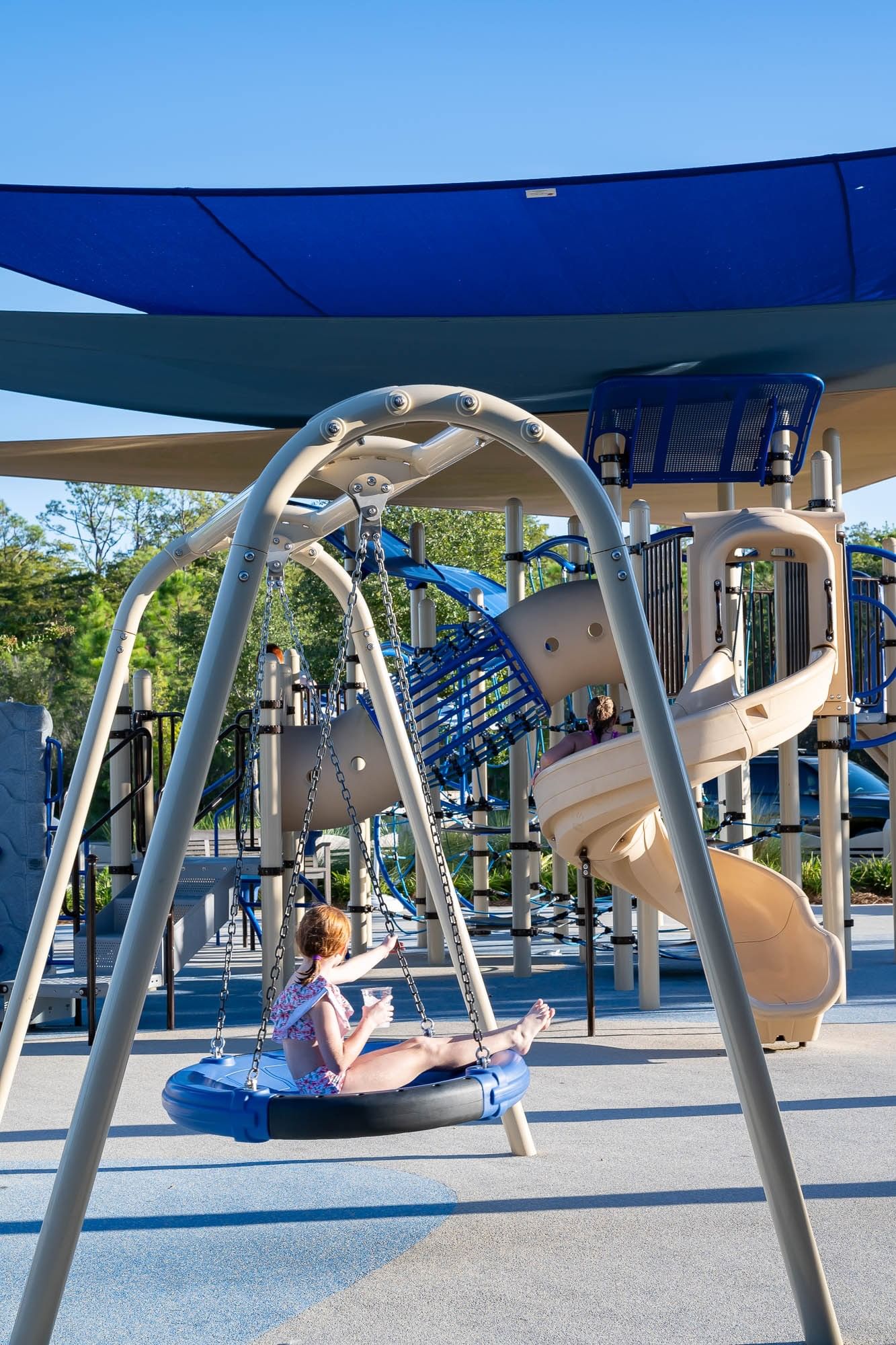 Child swinging on blue disc swing at modern playground with shade canopy and climbing structure at Camp Creek Inn