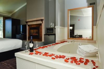 Superior King featuring a fireplace, a jetted tub with rose petals, and a wine bottle by the bed at Lake Natoma Inn