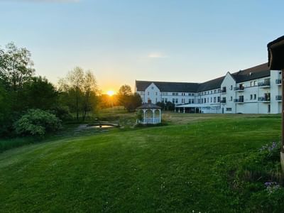 La Tourelle Hotel and Spa, featuring a distant facade view with a wooden gazebo on the lawn beneath a golden sunset