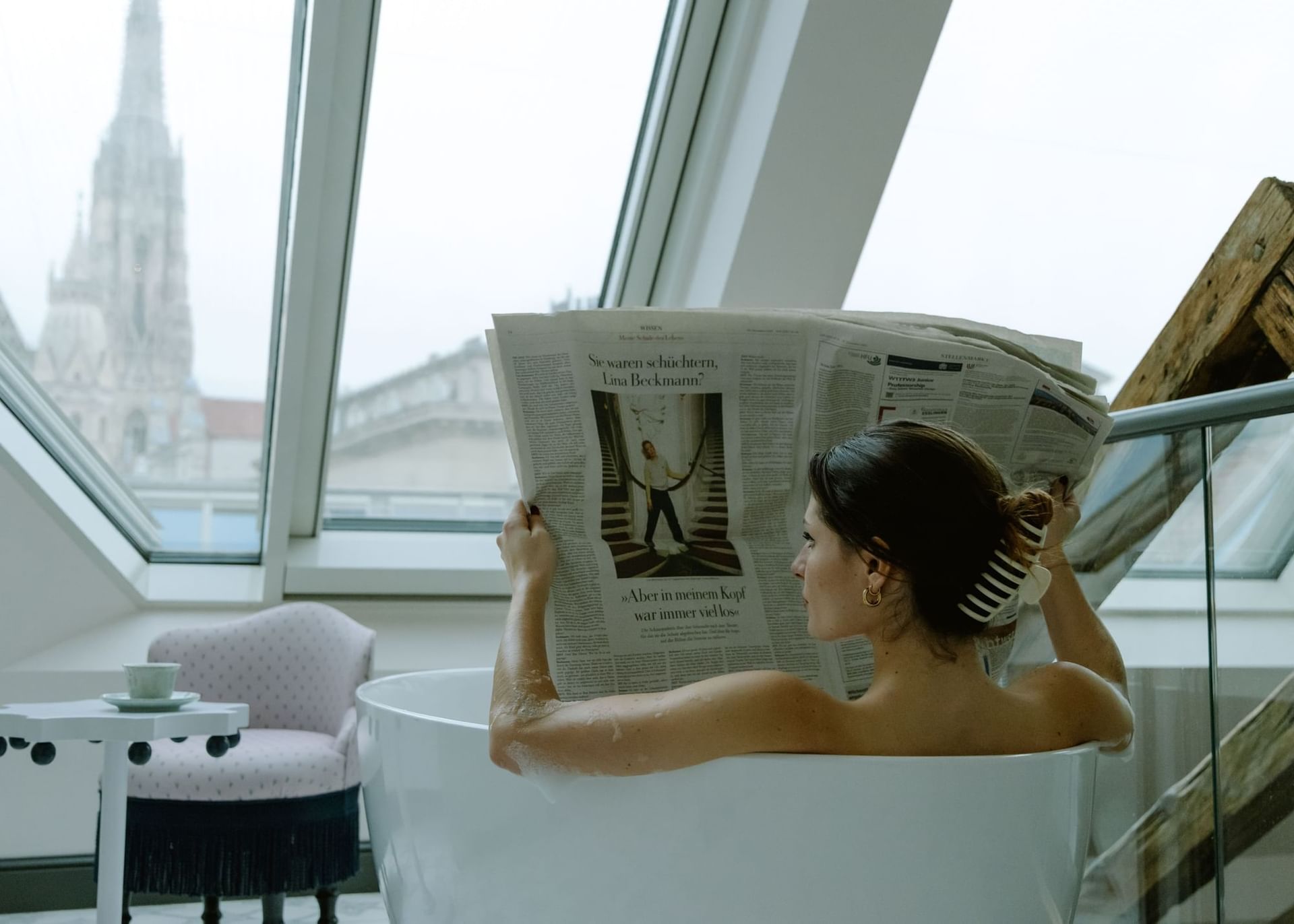 Frau sitzt in der Badewanne und liest eine Zeitung mit Stephansdomaussicht.