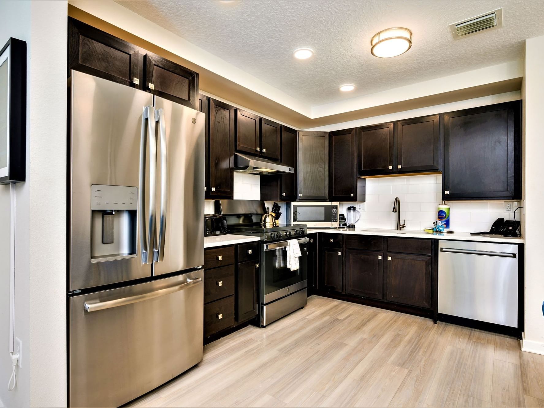 Modern kitchen with dark wood cabinets, stainless steel appliances, and light wood flooring at Vista Cay Resort By Millenium