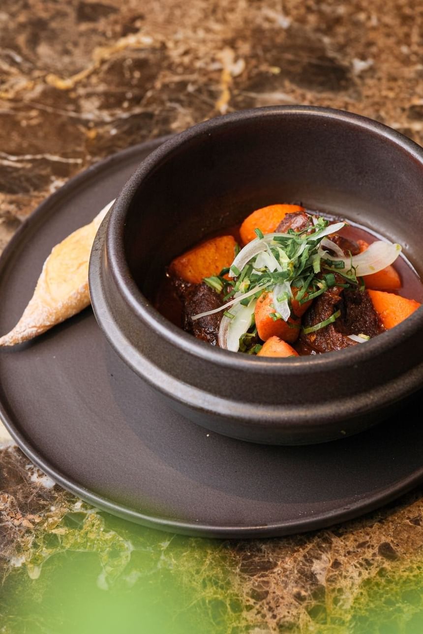 Stone bowl filled with tender beef, carrots, and herbs in a rich sauce, served with a side of bread at Park Hyatt Saigon