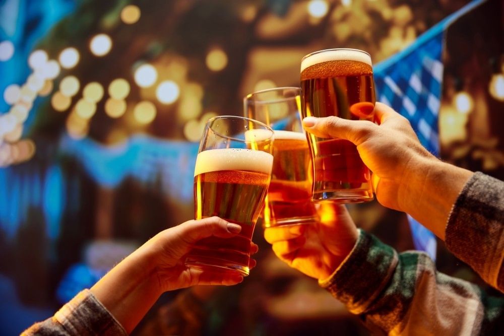Three hands toast with tall pint glasses of beer in a dim bar.