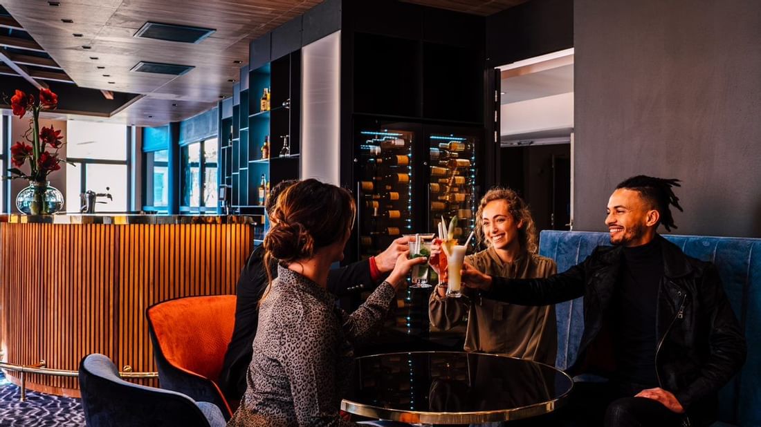 Trois personnes s'amusent en buvant des cocktails dans un bar élégant avec un plafond en bois.