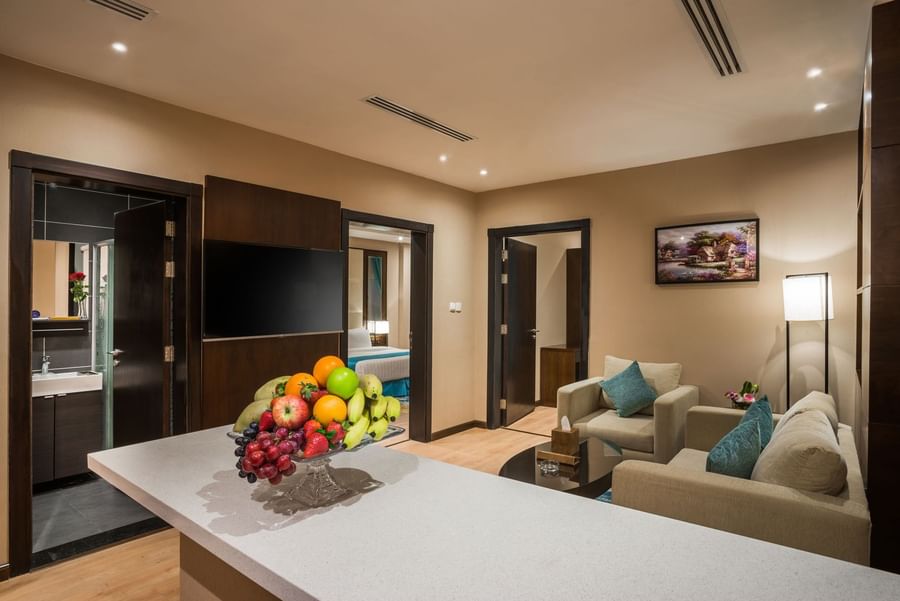 Fruit bowl on a counter by plush sofas and a TV under recessed lights in Family suite at Naviti By Warwick Dammam